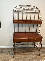 Front view of rustic bakers rack showing wood shelves, six small top drawers, two larger lower drawers, and decorative metal frame.