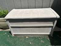 Front closed view of light gray resin patio storage box showing textured horizontal panel design.