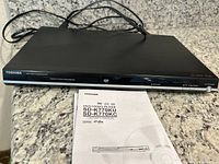 Full view of Toshiba DVD Video Player with owner's manual and power cables on granite countertop.