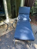 Front view of blue cushioned aluminum lounge chair next to round side table