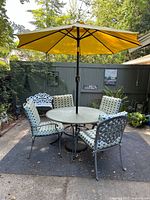 Patio table with yellow umbrella and four chairs with patterned cushions arranged on outdoor mat.