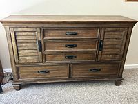 Front view of the wooden dresser showing three central drawers, two bottom drawers, and two side cabinets with horizontal shutter-style wooden doors fitted with metal handles.