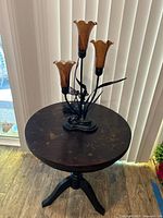 Round wooden side table with visible water stains and wear, displaying the Art Deco style lamp and decorative votive on top.
