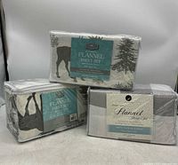Three new flannel sheet sets for twin beds in plastic packaging, showing different patterns and brand labels.
