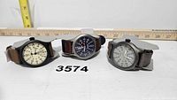 Three Timex watches arranged side by side with measuring rulers behind them showing sizes. Watches have different dial colors and leather straps.