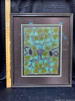 Front view of framed Aboriginal oil painting on canvas with a wooden ruler for scale, showing leafy organic shapes and dots in green, turquoise, black and white.