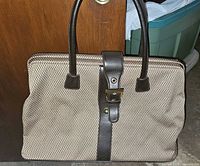 Weekender bag showing the brown and tan checkered pattern with dark brown leather handles and vertical strap with buckle.