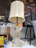 Full view of Asian-themed table lamp showing statue base, lampshade, and electrical cord coiled beside it.