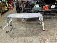 Full view of the Werner aluminum work bench with four legs and slatted top surface.