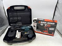 Black & Decker 18V drill, charger, battery pack, and carrying case arranged in plastic case, with 20V drill box beside them.