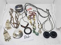 Lot of various necklaces including shell pendant, beaded styles, chain necklaces, and black circular earrings.