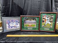 Three framed Philadelphia Eagles sports prints displayed on a black draped background with wooden and black frames and a measuring stick beneath for scale.