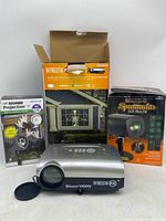 Front view showing all three projectors with their boxes: Window FX projector in silver with lens cap, Gemmy LED Lightshow Projection box, Holiday Time Spectacular Laser Projector box.