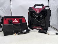 Dremel rotary tool, Husky drill bit case, and Husky carry bag arranged on white surface