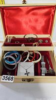 Jewelry box opened showing contents including bracelets, rings, necklaces, earrings, and watch inside red velvet lining