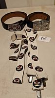 Two black leather belts with Shriners buckles and white suspenders with Shriners logos laid out on a table.