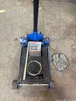 Top view of the blue hydraulic floor jack showing the handle, lifting platform with circular rubber pad, and warning label.