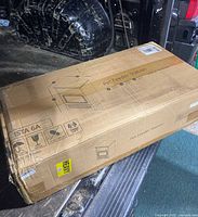 Wide view of the sealed cardboard shipping box for the pet feeder station, showing signs of wear and water damage on the lower edges.