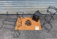 Lot contents showing one coir pinecone doormat and four black metal plant holders plus one black metal candle cage