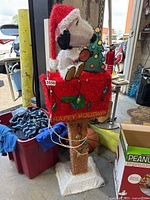 Front view of Snoopy sitting on a red, tinsel-covered mailbox decorated with Christmas lights and a small tree, showing the full height and details.