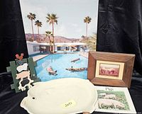 Photo showing the ceramic pig platter, framed pig print, pig-themed book, wooden pig photo holder, and a large photographic print with pigs floating in a pool.