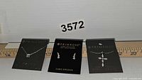 Three pieces of Primrose sterling silver jewelry displayed on branded black cards: two necklaces and one pair of earrings. All feature clear cubic zirconia stones.