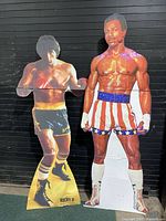 Full view of both Rocky II and Apollo Creed cardboard cutouts standing side by side showing condition and size.