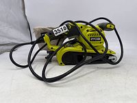 Side angle view of green Ryobi belt sander with handle, power cord, and sanding belt visible