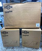 Three cardboard boxes labeled PetSafe ScoopFree, including one large litter tray box and two smaller litter boxes.