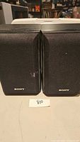 Front view of pair of Sony SS-B1000 bookshelf speakers showing black fabric grille and Sony logo with minor wear marks.