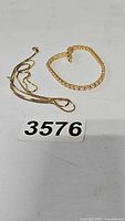 Goldtone sterling silver chain and tennis bracelet laid on white surface with lot number 3576.