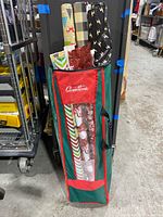 Side view of a green and red storage bag filled with wrapped rolls of Christmas wrapping paper showing varying heights and patterns.