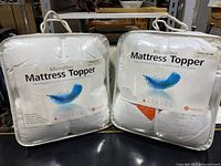 Two sealed microfiber mattress toppers for twin beds in white quilted fabric.