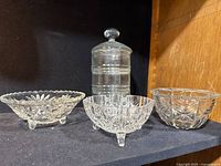 Three cut glass candy dishes and one apothecary jar on black shelf, showing overall set and designs.