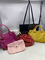 All six preowned ladies handbags and purses arranged together showing variety of colors and sizes.