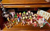 Wide view of various vintage Christmas ornaments and holiday small figures arranged on a wooden surface with some showing wear and tear.