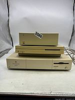 Front view of three Apple computer units stacked: Power Macintosh 6100/60 on bottom, Macintosh LC 575 middle, and external device on top. Two cables visible.