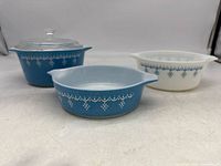 Three Pyrex baking dishes including one with glass lid, featuring white snowflake garland pattern on blue and white ceramic.