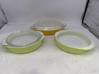 Three vintage Pyrex dishes: front lime green oval baking dish with lid, back yellow rectangular baking dish with lid, and right yellow round nesting serving dish without lid.