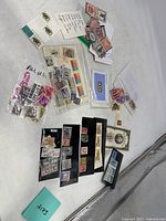 Multiple vintage postage stamps on black album pages and loose in bags spread on a white surface.
