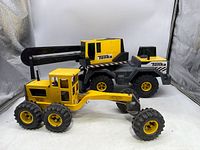 Yellow steel classic road grader and yellow and black Mighty Crane truck side by side showing construction toy design and condition