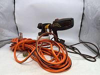 Wagner FLEXiO 570 paint sprayer alongside coiled orange extension cord on white background.