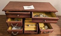Wood jewelry box with several drawers open showing assorted jewelry inside, including rings and bracelets.