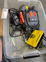 Overview of lot in clear plastic bin showing all battery devices, cables, tow ball