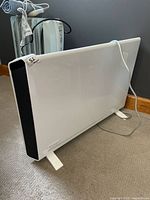 Front view of white DeLonghi Slim Style heater showing black side grille and attached feet