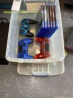 Top view of bin showing three DualShock 4 controllers and stack of six PS4 game cases