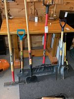 Five long-handled tools standing: rake, edger, ice chipper, snow shovel, garden shovel