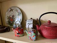 View of three teapots and a large decorative plate on shelf showing colors and details