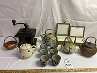 Photo of entire set showing four teapots, six teacups, vintage coffee grinder, and small basket