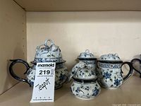 Full view of the blue and white floral ceramic tea set pieces including teapot, sugar bowl, creamer, and an additional lidded piece all displayed together on shelf.